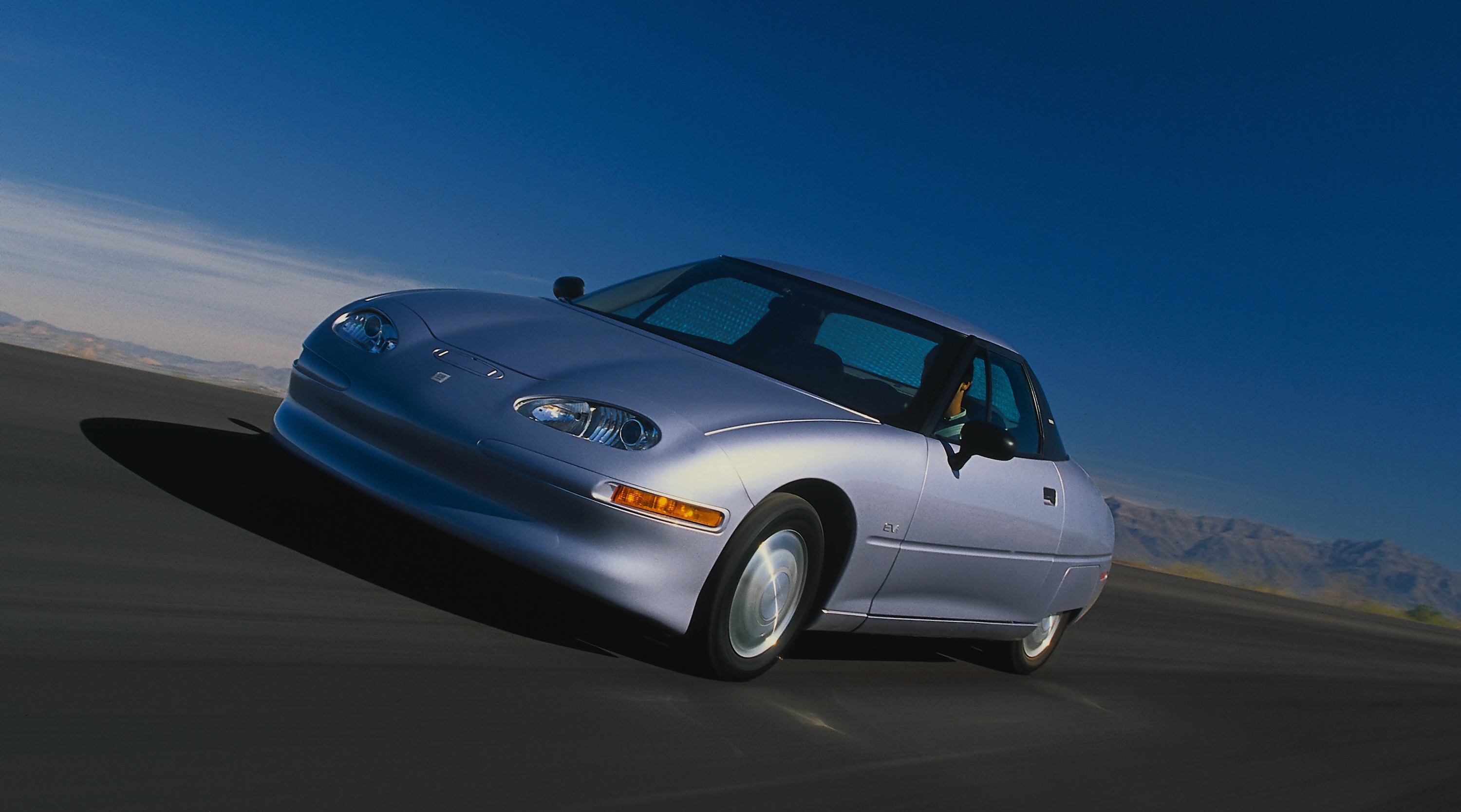 The GM EV1 electric car driving across a dark road at dusk
