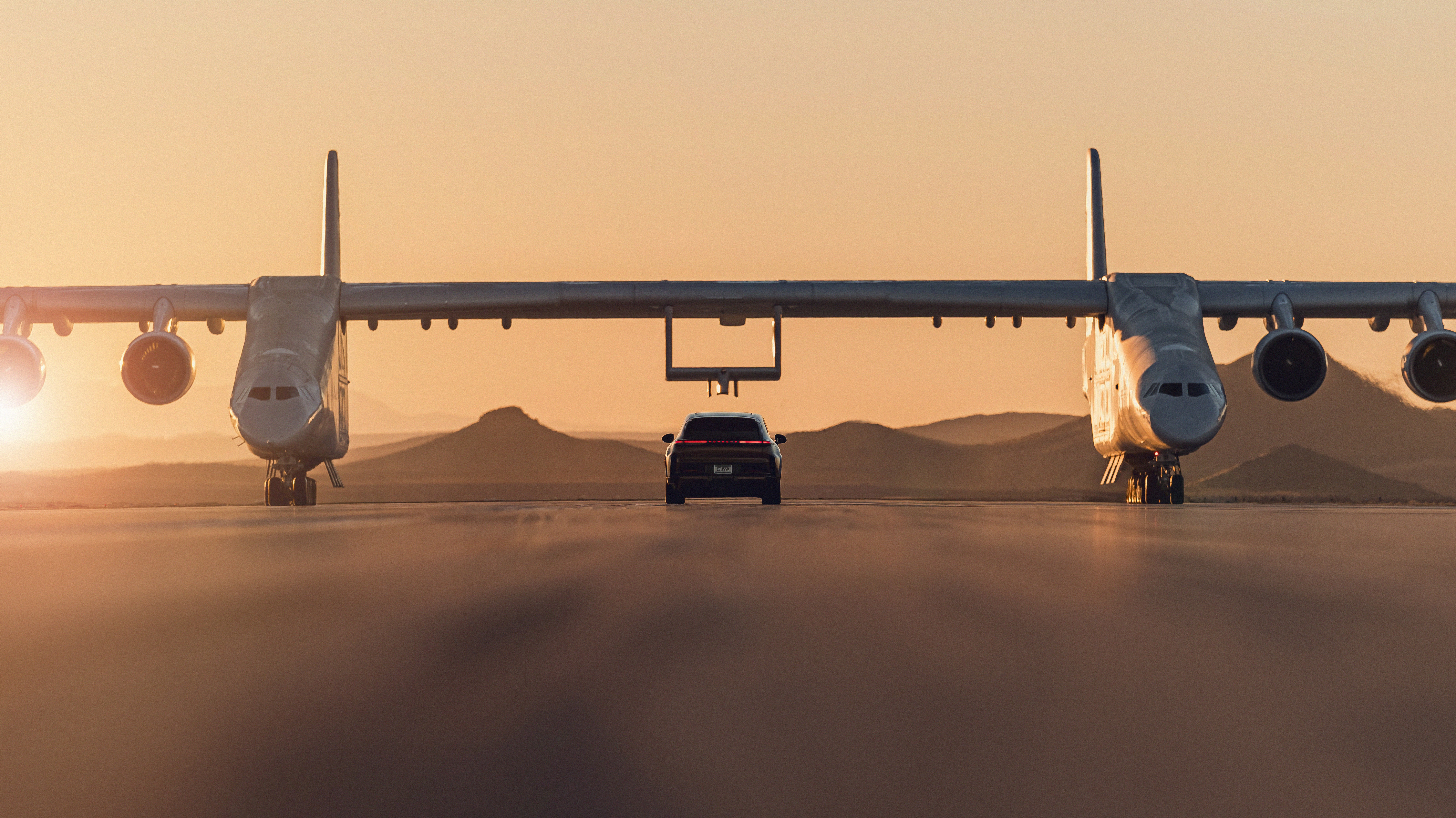 Porsche Cayenne Turbo Electric driving beneath Stratolaunch’s Roc aircraft on a runway